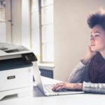 Junge Frau, die an ihrem Computer neben einem Multifunktionsdrucker Xerox® B315 arbeitet.
