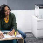 Lächelnde Frau in einem Büro neben dem Xerox® VersaLink® C620 Farbdrucker