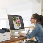 Eine Frau sitzt an einem Schreibtisch, konzentriert auf ihre Arbeit, mit einem Xerox® C320 Farbdrucker Eine Frau sitzt an einem Schreibtisch, konzentriert auf ihre Arbeit, mit einem Xerox® C320 Farbdrucker